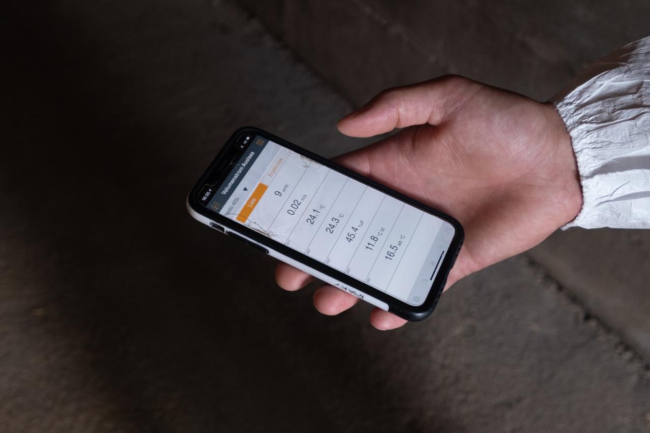 Handy in der Hand einer Person, verschiedene Stallklimawerte auf dem Bildschirm zu lesen.